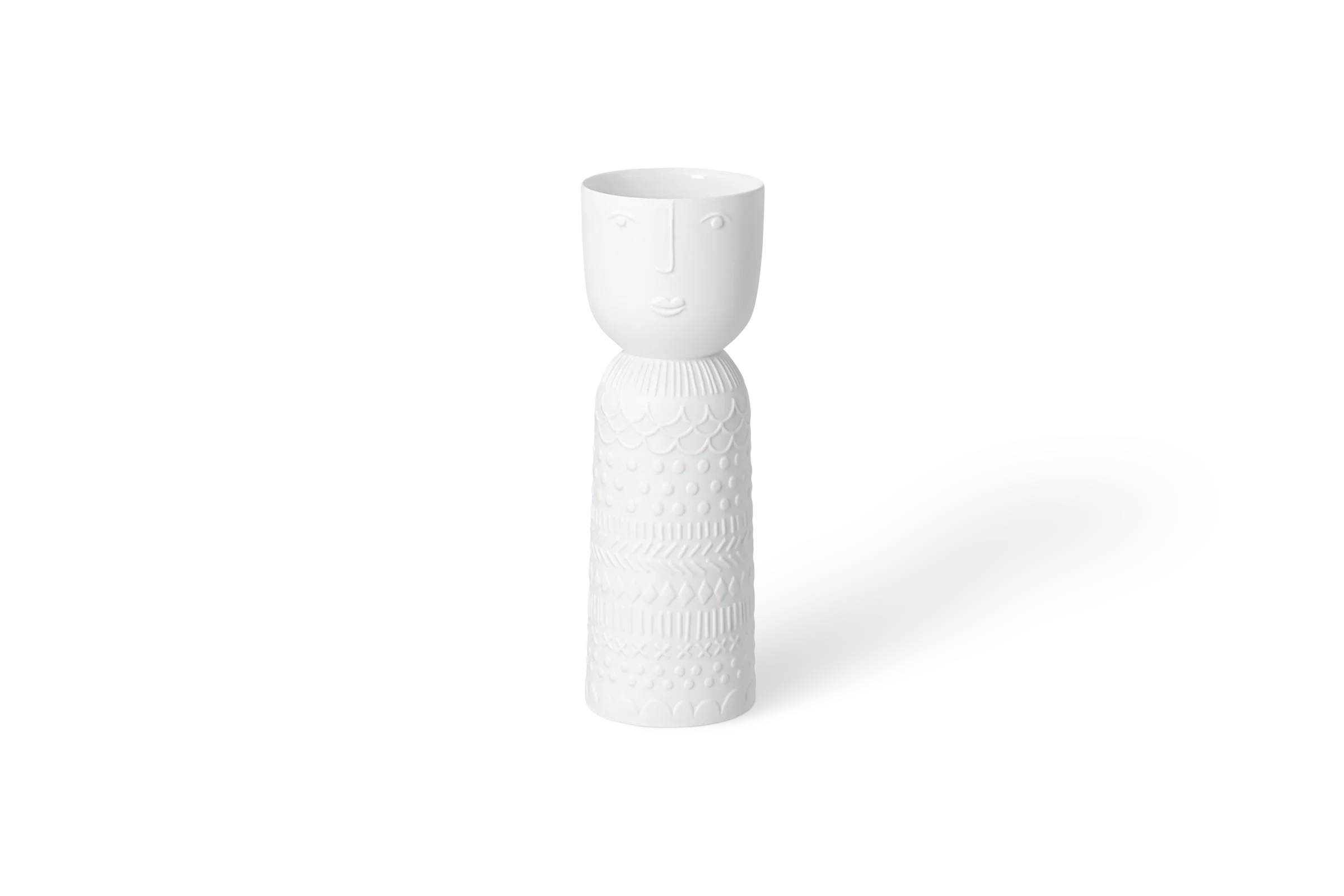 Kerzenhalter Lichtgestalt Lucia Weißer Kerzenhalter in Figurenform mit Gesicht und erhabenen geometrischen Mustern, in der Vorderansicht.