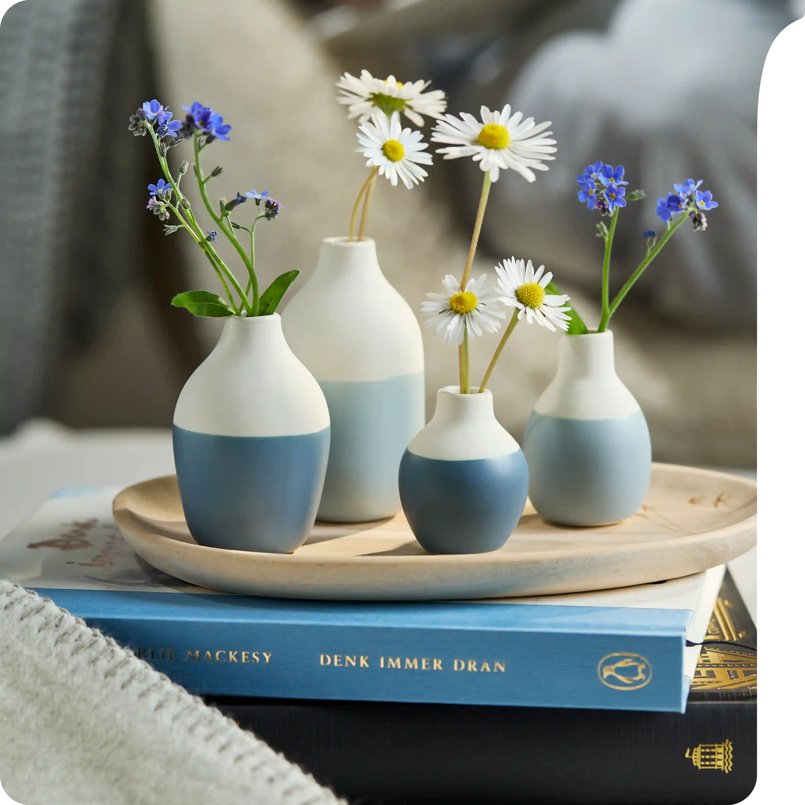 Minivasen Flaschen Blau - 4er Set Vier blau-weiße Minivasen mit Gänseblümchen und Vergissmeinnicht auf einem Tablett.