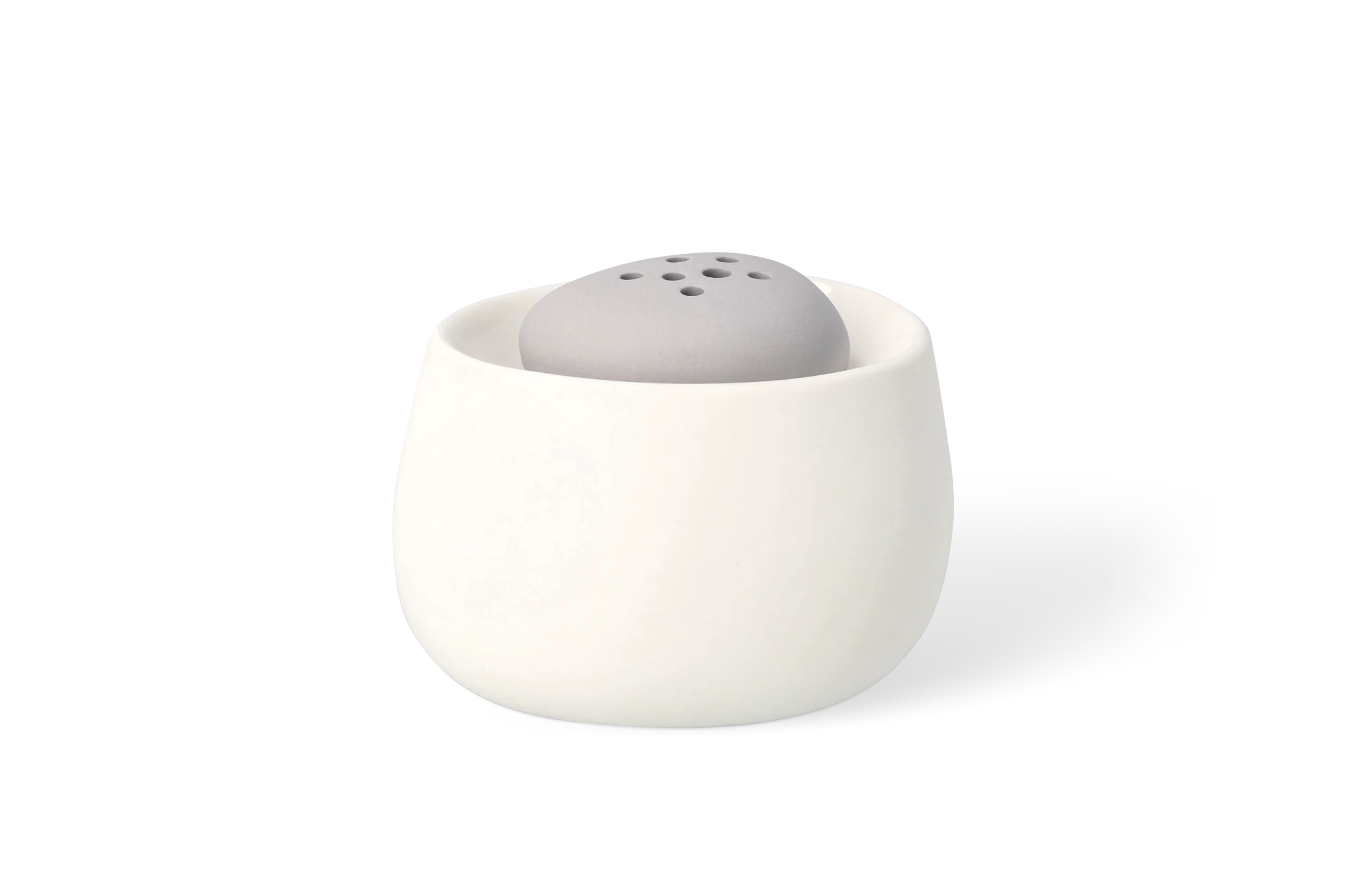 Weiße Minivase mit grauem, gelochtem Einsatz in Kieselsteinform, in der Ansicht von hinten links.